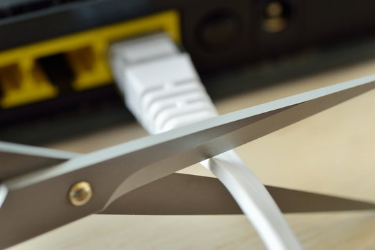 Scissors cutting internet modem router cable - Concept of network and data protection