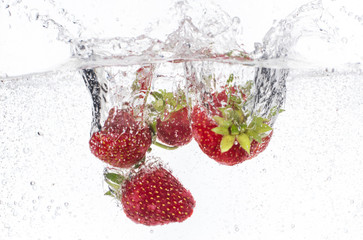 ripe red strawberries are thrown and dropped into sparkling water, many bubbles