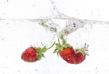 ripe red strawberries are thrown and dropped into sparkling water, many bubbles