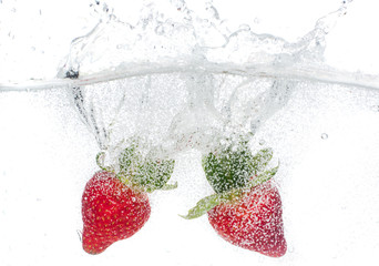 ripe red strawberries are thrown and dropped into sparkling water, many bubbles