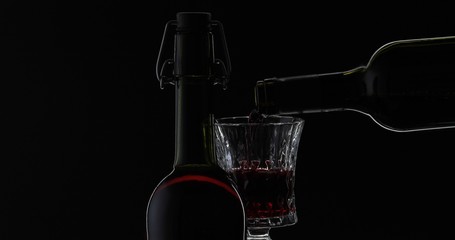 Rose wine. Red wine pour in wine glass over black background. Silhouette