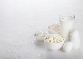 Fresh dairy products on white table background. Glass of milk, bowl of baking flour, cottage cheese and mozzarella. Eggs and cheese. Space for text