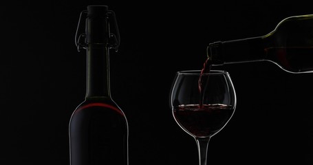 Rose wine. Red wine pour in wine glass over black background. Silhouette