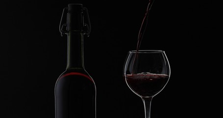 Naklejka na ściany i meble Rose wine. Red wine pour in wine glass over black background. Silhouette