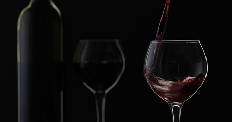 Rose wine. Red wine pour in wine glass over black background. Silhouette