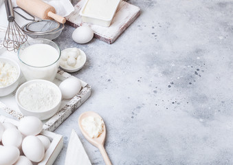 Fototapeta na wymiar Fresh dairy products on white table background. Glass of milk, bowl of flour and cottage cheese and eggs. Box of baking utensils. whisk and spatula in vintage wooden box.Top view. Space for text