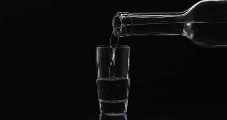 Pouring up shot of vodka from a bottle into glass. Black background