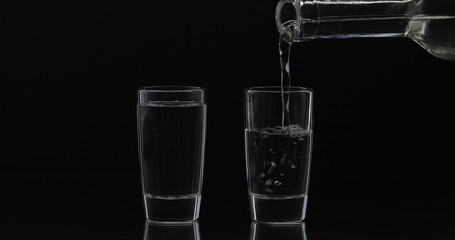 Pouring up shot of vodka from a bottle into glass. Black background