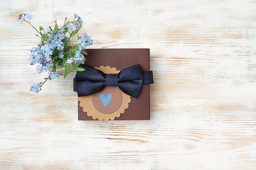 blue forget-me-not flowers and gift box with tie-bow for Dad on light background. concept gift for dad, men, brutal style.  father's day holiday background. top view