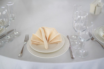table setting, glasses are on the table, napkins in napkins beige, appliances fork knife, white clean plates, the table is set before the event