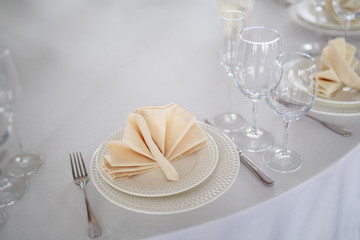 table setting, glasses are on the table, napkins in napkins beige, appliances fork knife, white clean plates, the table is set before the event