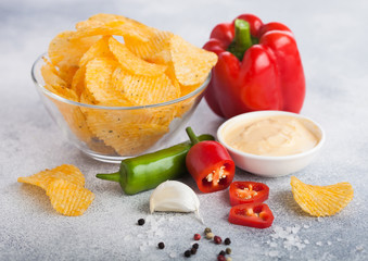 Glass bowl plate with potato crisps chips with chilli pepper on light table background. Red and green chilli pepper with garlic and salt.