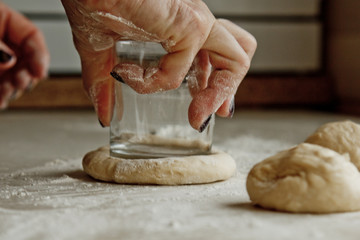 women's hands cut the raw kneaded dough into pieces on the background of the kitchen interior. cooking baking dish