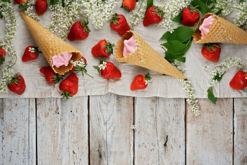 Strawberry ice cream in waffle cones surrounded by fresh strawberries and bird cherry blossoms. Summer frame. Top view