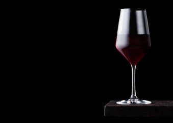 Glass of red wine on wooden board on black background. Space for text