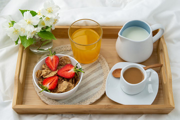 Breakfast in bed. Wooden tray with coffee,orange juice, strawberries and muesli . Jewelry with delicate white flowers.