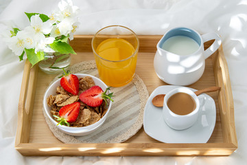 Breakfast in bed. Wooden tray with coffee,orange juice, strawberries and muesli . Jewelry with delicate white flowers. Beautiful sunlight.