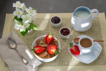 Light Breakfast coffee with milk and muesli, fresh strawberries, jam. Decoration of white delicate flowers. Beautiful sunlight.