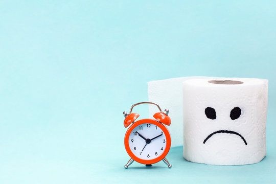 Concept of constipation, indigestion, digestion problem. Alarm clock and toilet paper with sad face