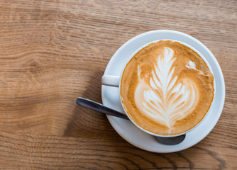 One cup of cappuccino with latte art on wooden table, white ceramic cup, top view. Cafe culture.