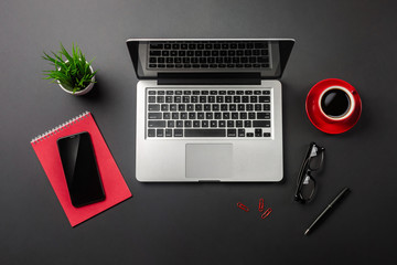 Black office desk table with blank screen laptop computer, notebook, mobile phone and red cup of coffee