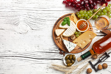 White wine bottle, grape, honey, cheese and wineglass on white wooden board