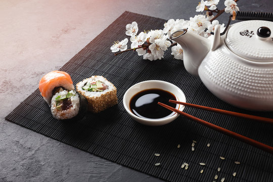 Set of sushi and maki rolls with branch of white flowers and teapot with the inscription green tea on stone table