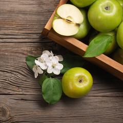 Ripe green apples with branch of white flowers in wooden box on a wooden table