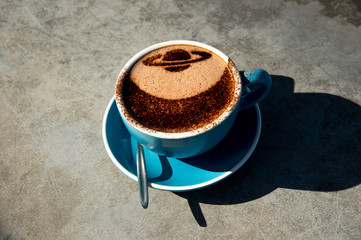 Close up blue a cup of hot chocolate with cocoa powder Saturn shape decoration and shadow on cement...