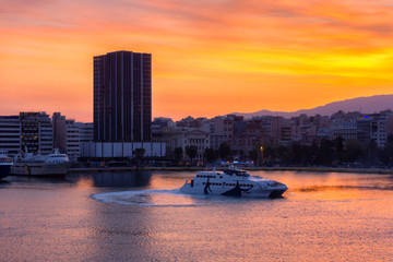 Piraeus Port, Attica / Greece. Colorful sunrise with fiery sky over the port and the city of Piraeus. Seajets vessel is making manoeuvring at the port