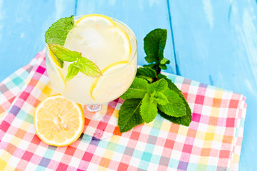 Lemonade with ice and lemon slices and mint in a glass on a blue wooden table. Summer cold refreshing drink with fruits and vitamins.
