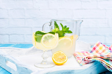 Lemonade with ice, lemon slices and mint in a glass and a carafe on a blue wooden table. Summer...