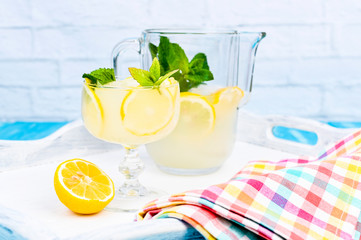 Lemonade with ice, lemon slices and mint in a glass and a carafe on a blue wooden table. Summer...