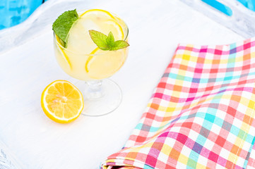 Lemonade with ice and lemon slices and mint in a glass on a blue wooden table. Summer cold refreshing drink with fruits and vitamins.