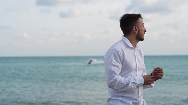 Portrait of happy bearded man standing near the sea. Young guy stands serenely on the seashore.