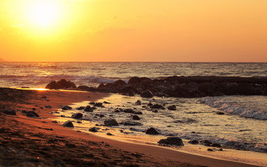 Sunset on wild beach, sun shines on wet stones in sand.