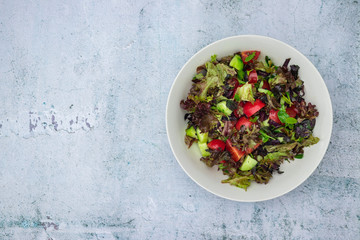Fresh summer salad and avocado pieces on white marble background with space for text. Vegan, vegetarian healthy food.
