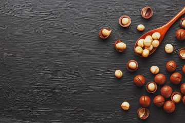 Shelled macadamia nut and peeled macadamia nut on a black textural background in a wooden spoon. Low contrast
