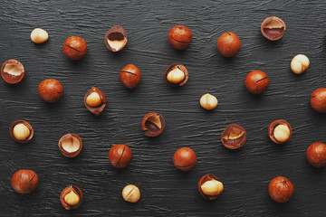 Fototapeta na wymiar Purified and shell repeats macadamia nuts on black textural stone background. Healthy eating concept. Low contrast
