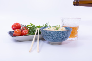 Noodles In A bowl with Fresh salad, a beer and chopsticks. White background