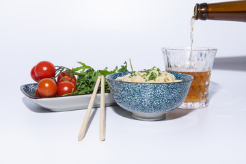 Noodles In A bowl with Fresh salad, a beer and chopsticks. White background