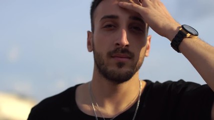 Portrait of a young guy fixing his hair with his hand close up. Handsome unshaved man touch thick dark hair.