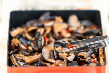 Traditional marinated shiitake mushrooms for sampling or buying in Takayama morning market with stainless steel made in Japan tongs macro closeup and sign