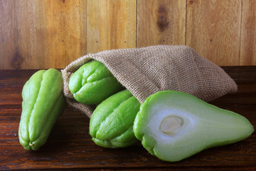 raw, fresh and organic chayote, whole and sliced in rustic bag on wooden table