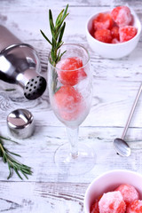 A glass with watermelon ball shaped pieces and rosemary is ready to be filled with a drink
