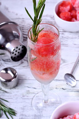 Sparkling cocktail with watermelon balls and rosemary in a champagne glass on white table