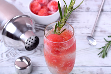 Sparkling cocktail with watermelon balls and rosemary in a champagne glass on white table