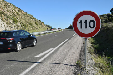 Panneau vitesse limitée à 110 au bord d'une route à quatre voies
