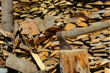 An ax impaled on a stump against the background of firewood in the sarp