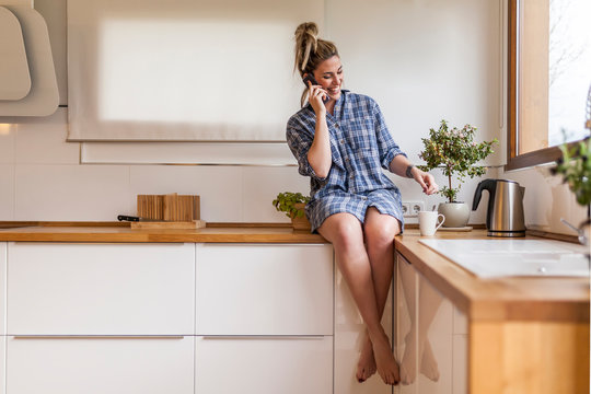 beautiful and young woman having breakfast at home and having fun, sitting on the kitchen and talking on the phone